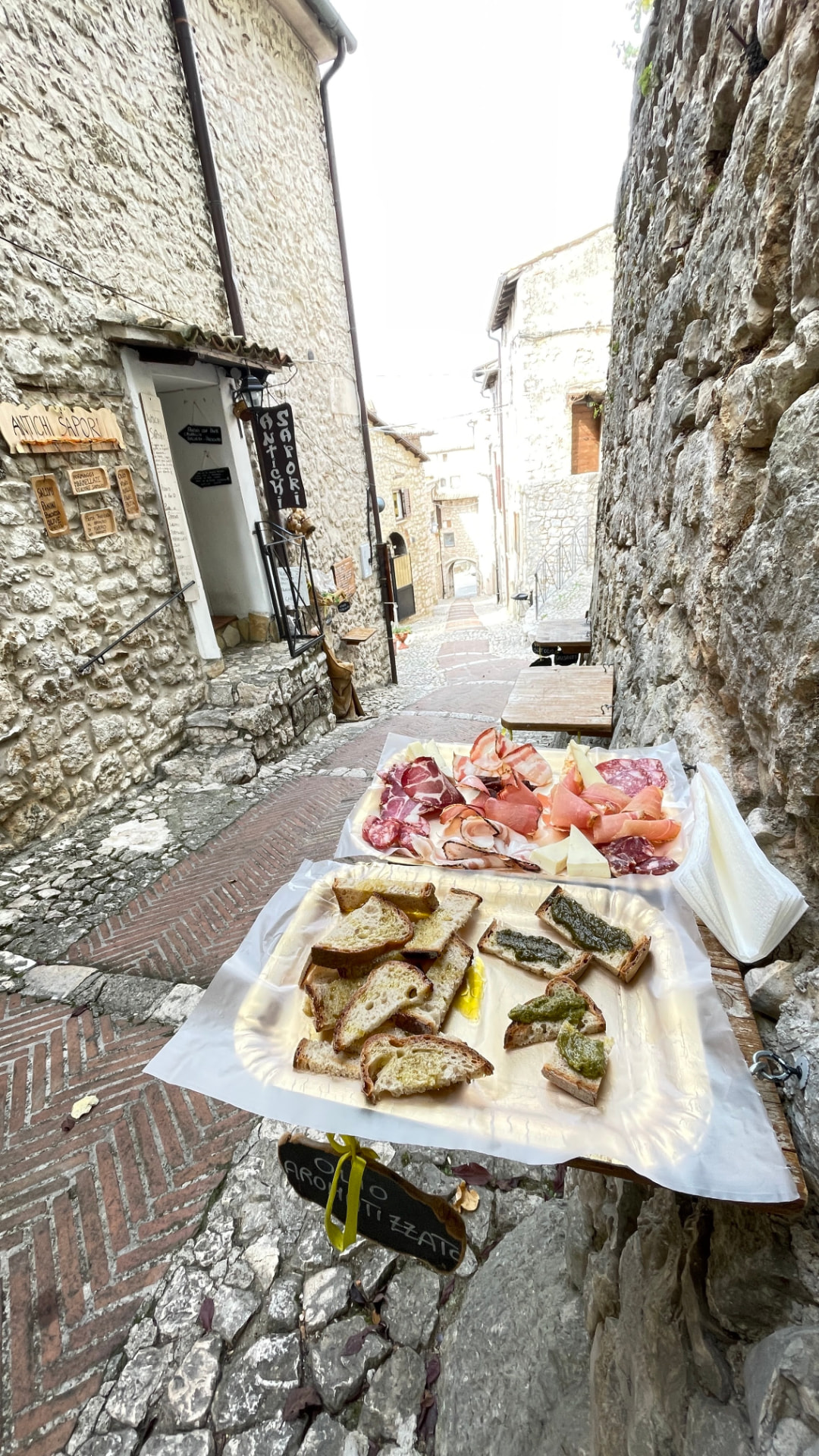 Fade med spegepølser, ost og bruschetta på et bord i en stenbelagt gyde i Fumone